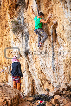 Young man lead climbing on natural cliff, belayer watching him