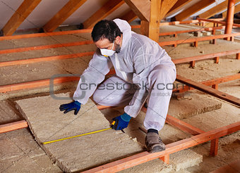 Man laying thermal insulation layer under the roof