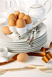 Eggs in white egg cups on a pile of plates with ribbons