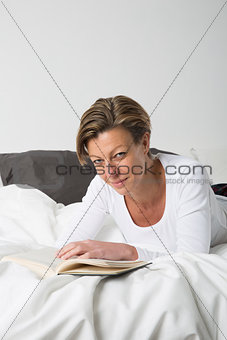 Smiling Woman reading a book in bed