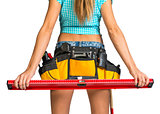 Woman wearing tool belt with tools holding builders level, close up