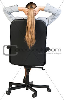 Businesswoman sitting back in office chair with hands clasped behind her head. Back view