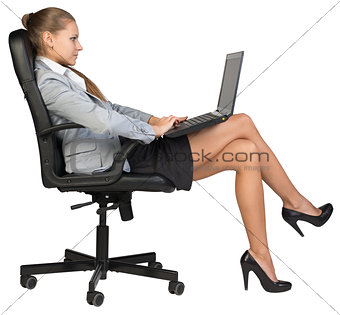 Businesswoman sitting back in office chair, with laptop on her knees