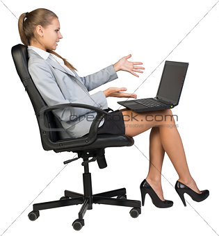 Businesswoman on office chair with laptop, looking and pointing at the blank screen