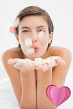 Composite image of beautiful happy woman blowing flower petals at spa center