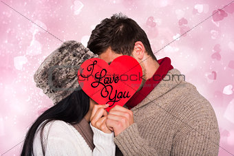 Composite image of young couple kissing behind red heart