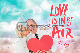 Composite image of older affectionate couple holding red heart shape