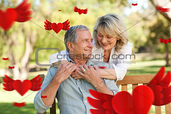 Composite image of senior woman hugging her husband who is on the bench