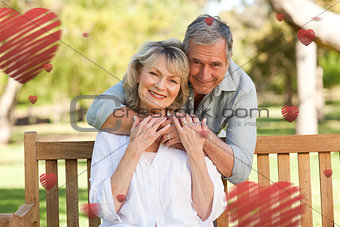 Composite image of elderly man hugging his wife who is on the bench
