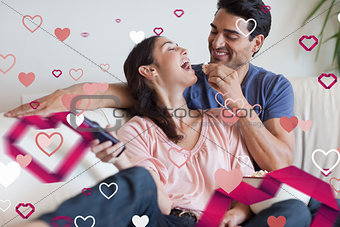 Composite image of playful couple watching tv while eating popcorn
