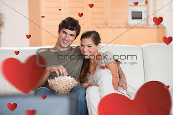 Composite image of couple with popcorn on the sofa watching a movie