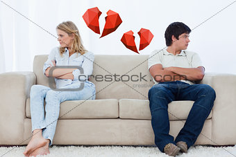 Composite image of a couple sit at the two ends of the couch with their arms folded looking away