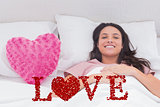 Composite image of woman lying in her bed next to a pink heart pillow