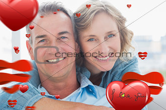Composite image of smiling woman hugging her husband on the couch from behind