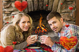 Composite image of couple with tea cups in front of lit fireplace
