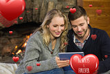 Composite image of couple using tablet pc in front of lit fireplace