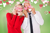 Composite image of silly couple holding hearts over their eyes