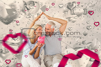 Composite image of happy couple sitting and sheltering piggy bank