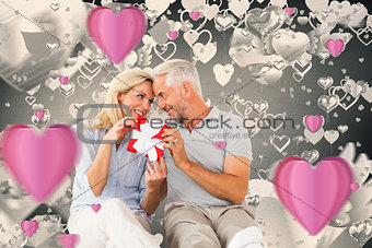 Composite image of happy couple sitting and holding present