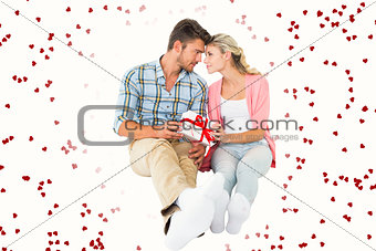 Composite image of attractive young couple sitting holding a gift