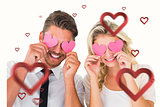 Composite image of attractive young couple holding pink hearts over eyes