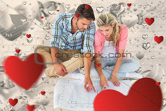 Composite image of attractive young couple sitting looking at blueprint