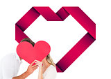 Composite image of attractive young couple kissing behind large heart
