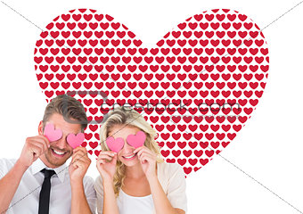 Composite image of attractive young couple holding pink hearts over eyes