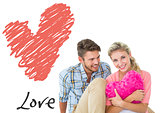Composite image of attractive young couple sitting holding heart cushion