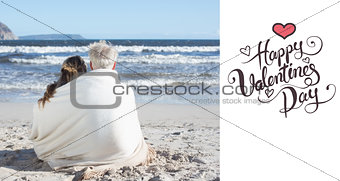 Composite image of couple sitting on the beach under blanket looking out to sea