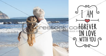 Composite image of couple wrapped up in blanket on the beach looking out to sea