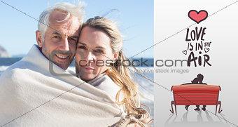 Composite image of smiling couple wrapped up in blanket on the beach