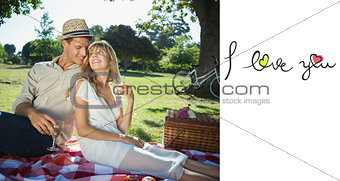 Composite image of cute couple drinking white wine on a picnic smiling at each other