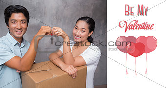 Composite image of happy couple holding house key and leaning on moving box