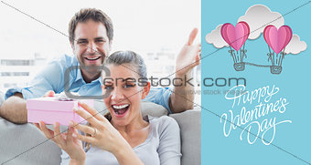 Composite image of man surprising his delighted girlfriend with a pink gift on the sofa
