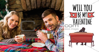 Composite image of smiling couple with tea cups in front of lit fireplace