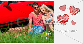 Composite image of smiling couple sitting on the grass having picnic together