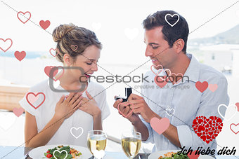 Composite image of man surprising woman with a wedding ring at lunch table