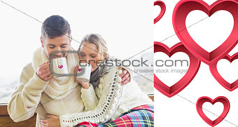Composite image of loving couple in winter wear drinking coffee against window
