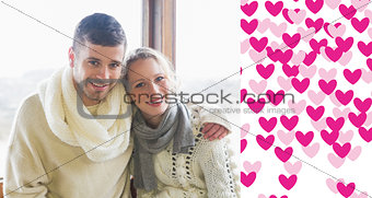 Composite image of couple in winter clothing sitting against window