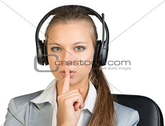 Businesswoman in headset holding finger to her lips