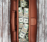 suitcase full of dollars on a wooden background. view from above