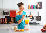 Happy fitness young woman making pumpkin smoothie in kitchen