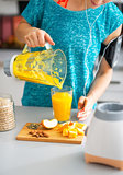 Close-up on fitness young woman pouring pumpkin smoothie in glas