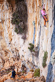 Young woman lead climbing on natural cliff, belayer watching her