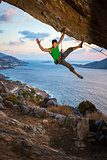 Cheerful rock climber waving his hand while climbing at sunset