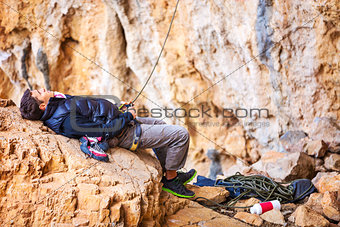 Young man lying on stone and watching leading rock climber while belaying