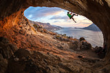 Male rock climber climbing along a roof in a cave at sunset