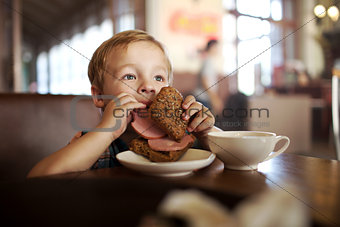 Little child having lunch with sandwich and tea in cafe