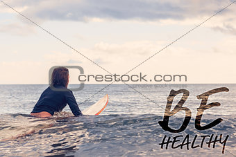 Composite image of rear view of a woman sitting on surfboard in water